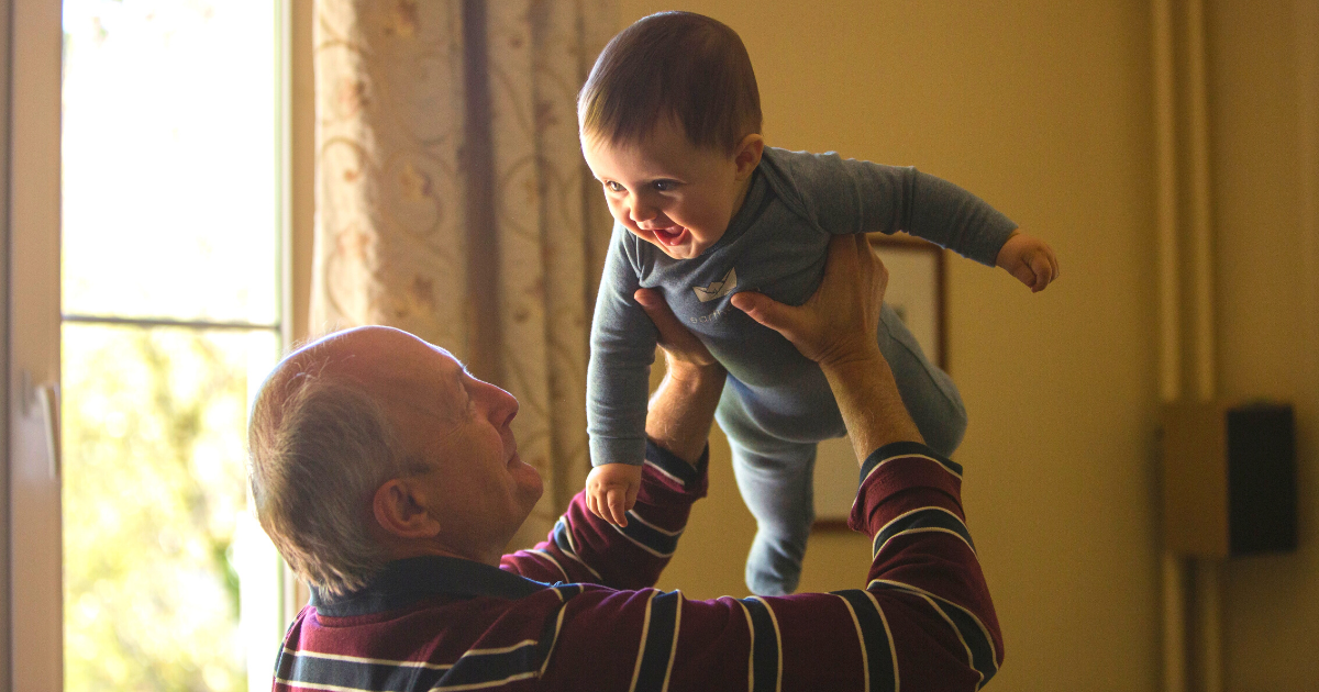 grandfather holding up laughing and smiling baby